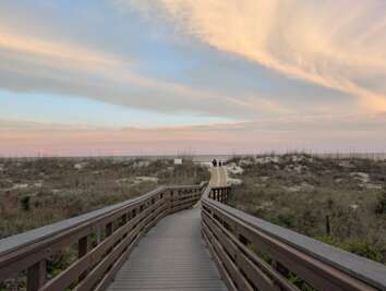 A wooden boardwalk leads through grassy dunes towards the...