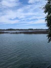 Tranquil water stretches out under a wide, partly cloudy sky,...