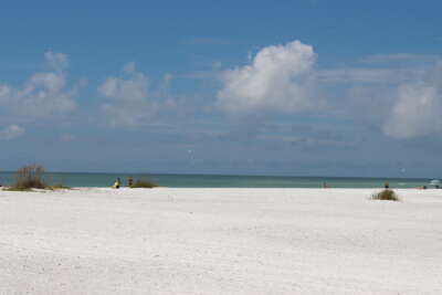 A broad expanse of white sand stretches towards a calm...