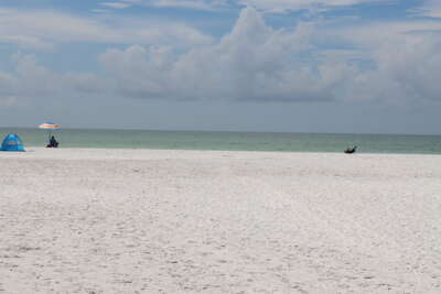 A vast stretch of white sandy beach under a cloudy sky, with...