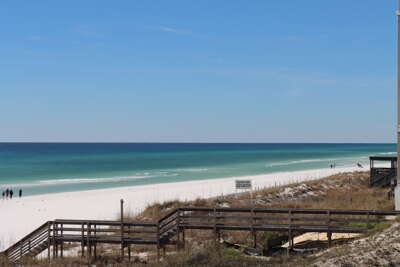 A wooden boardwalk leads toward a serene, white sandy beach...