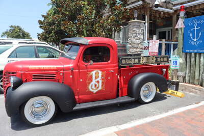 A vibrant red vintage truck is parked outside a tavern and a...
