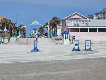 A paved beachside promenade leads towards a bustling boardwalk...