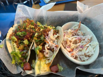 A meal featuring two filled tacos next to a bowl of slaw served...