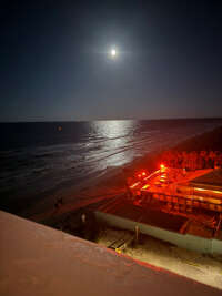 A terrace overlooks a night-lit shore where people gather under...