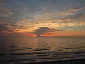 A serene sunset casts hues of orange and purple over the ocean,...