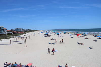 Beachgoers enjoy a sunny day on Oak Island, NC a wide, sandy...
