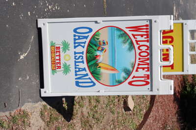 A sign welcomes visitors to Oak Island, NC featuring a tropical...