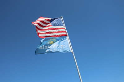 Two flags wave against a clear blue sky, with one featuring the...