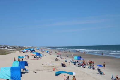 Beachgoers relax under colorful canopies along Ocean Isle...
