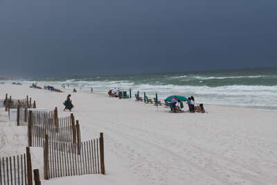 A sandy beach on Okaloosa Island, FL stretches under a cloudy...