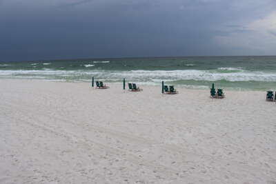 Rows of green beach chairs are lined up on a white sandy beach...