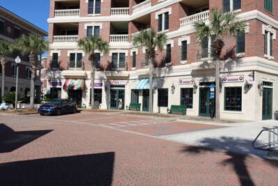 A sunlit plaza flanked by multi-story buildings and palm trees...