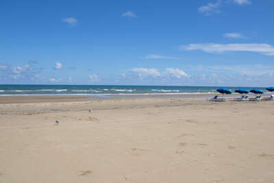 A sandy beach stretches under a vast blue sky, punctuated by...