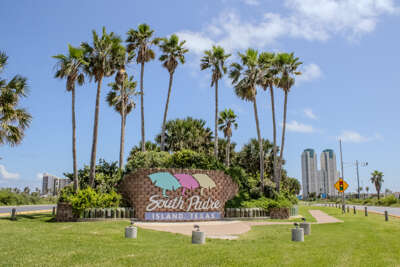 Tall palm trees frame a colorful welcome sign for South Padre...