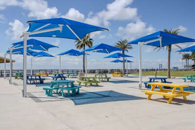 Picnic tables shaded by blue umbrellas await visitors seeking...