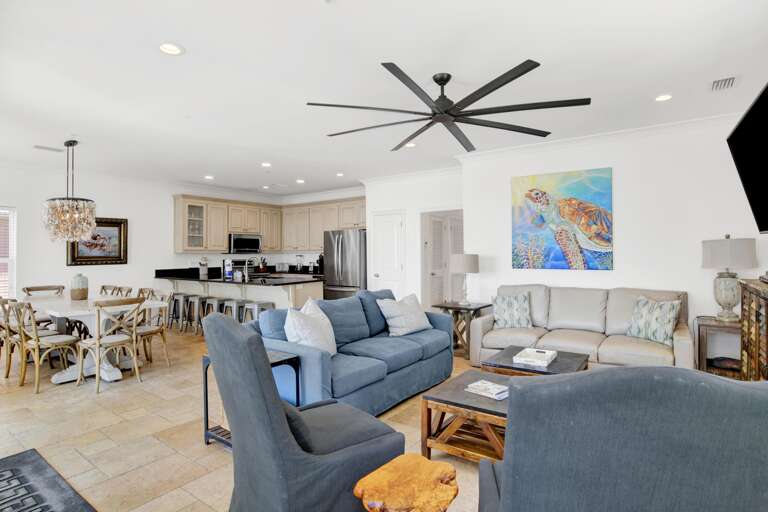 Open-plan living and dining area with blue and gray sofas, wood coffee tables, cream cabinetry, and tile flooring.
