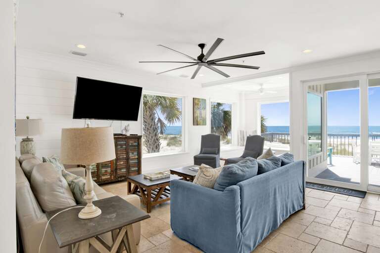 TV mounted above a rustic multicolor wood cabinet, with beige and blue sofas arranged around dark wood coffee tables.