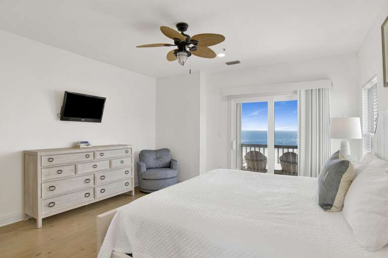 King bed with white quilted bedding faces sliding glass doors leading to a balcony with ocean views.