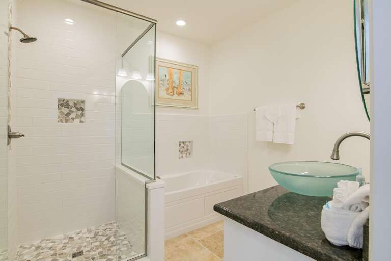 Bathroom with glass vessel sink on black granite countertop, walk-in shower with mosaic tile floor, and white soaking tub.