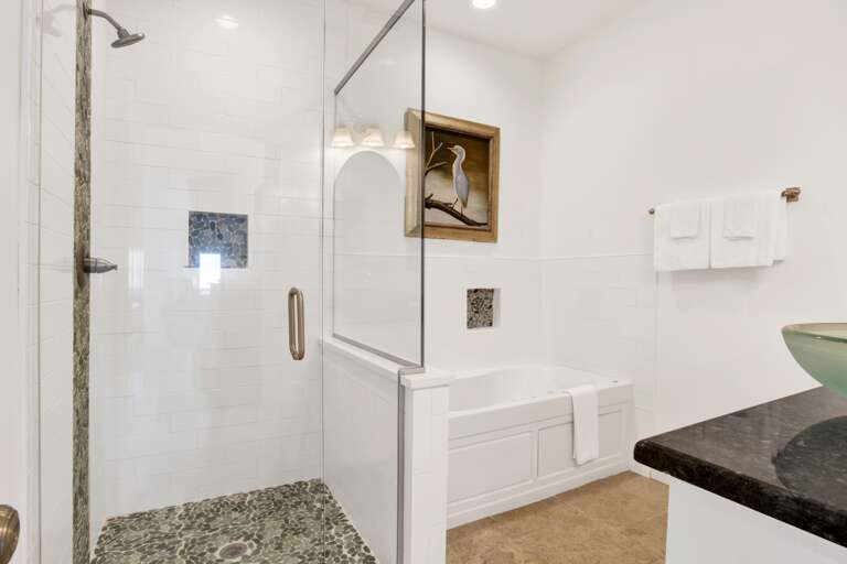 Bathroom with pebble-tile shower floor, glass partition, white soaking tub, and green glass vessel sink.