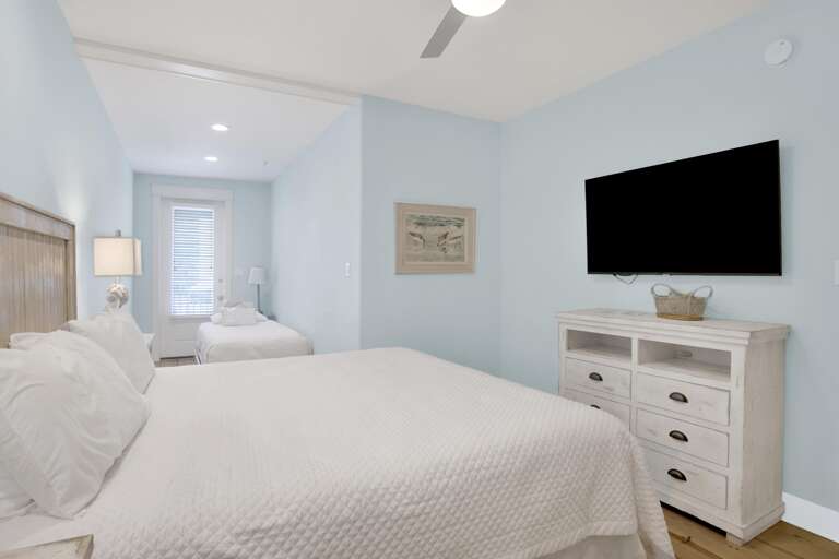 Bedroom with pale blue walls, white wooden dresser under wall-mounted flat screen, and two beds with white quilts.