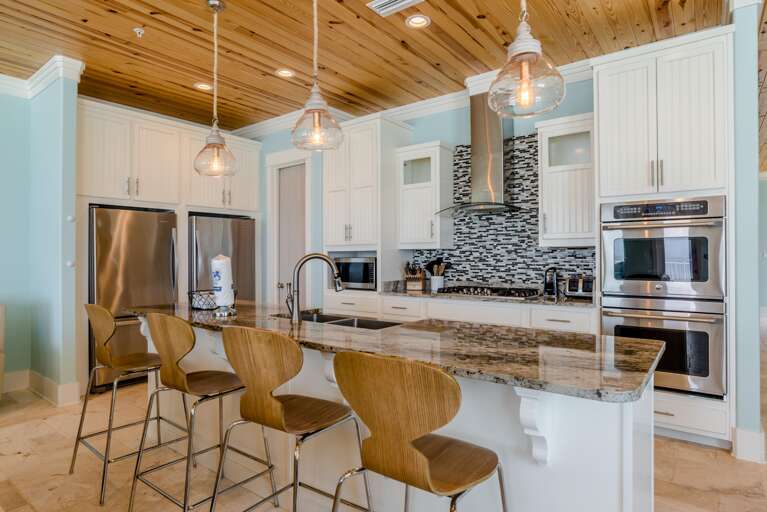 Stainless steel double ovens and gas cooktop sit beneath a glass and stone mosaic backsplash in the kitchen.