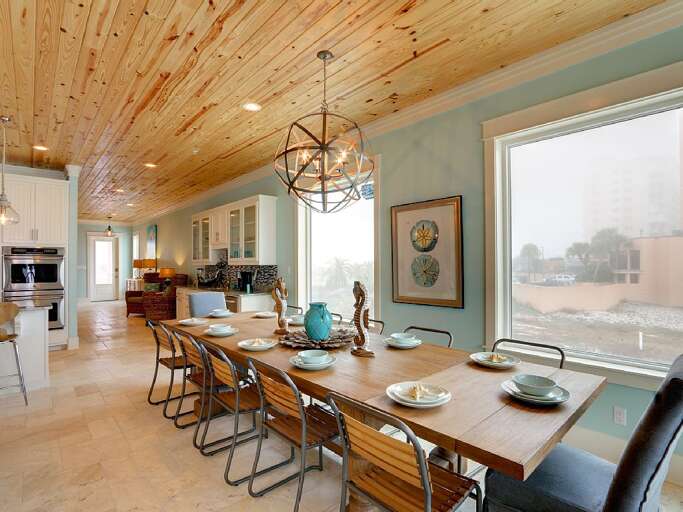 Long wood dining table set with plates and bowls beneath a wood plank ceiling and metal orb chandelier.