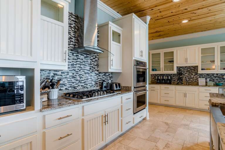 Kitchen features granite countertops, white cabinetry with glass panels, mosaic tile backsplash, and stainless appliances.