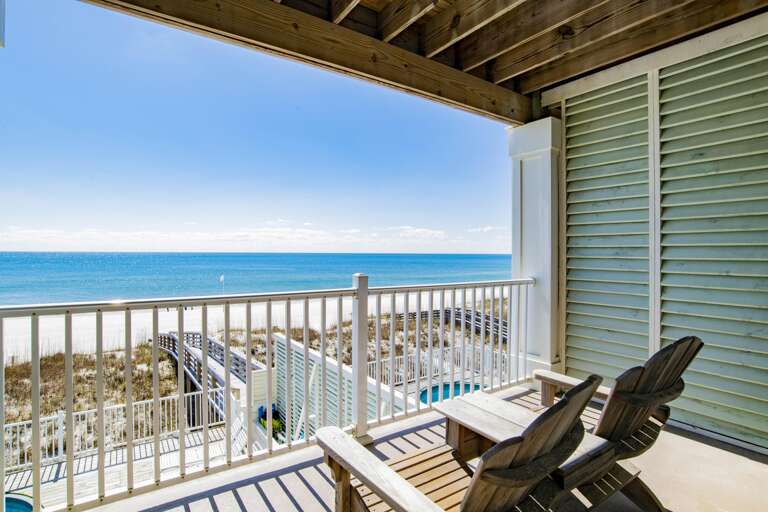 Private balcony with weathered Adirondack chairs, white metal railings, and unobstructed views of the sandy beach and turquoise gulf.