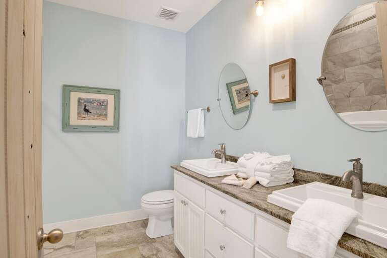 Bathroom with dual rectangular sinks, granite countertop, pale blue walls, and two round mirrors above.