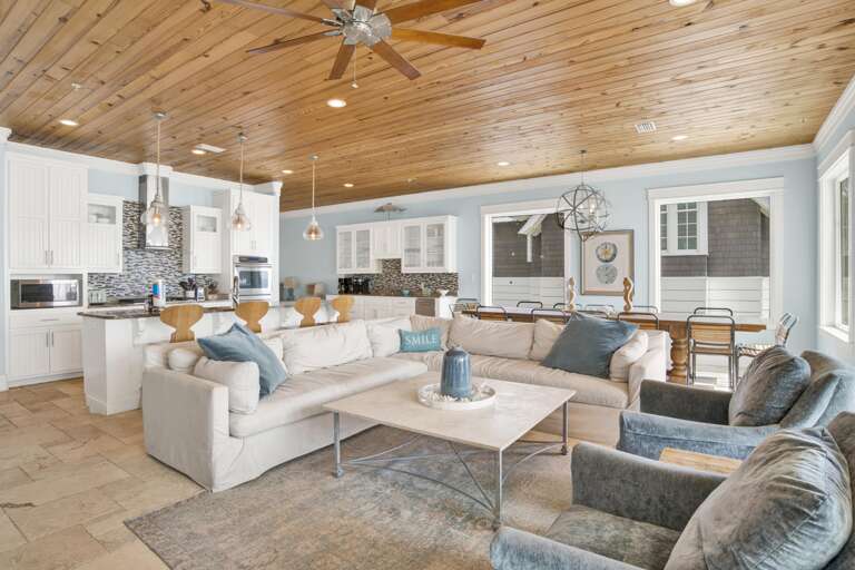 Living room with large cream sectional, blue-gray armchairs, and wood-paneled ceiling with ceiling fan and recessed lighting.
