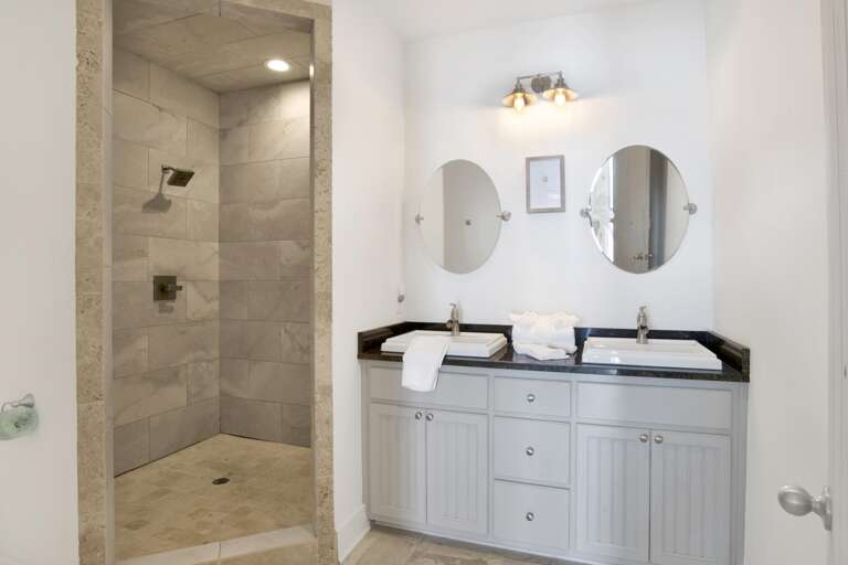 Bathroom features a dual-sink vanity with black granite countertop and a tiled walk-in shower with stone trim.
