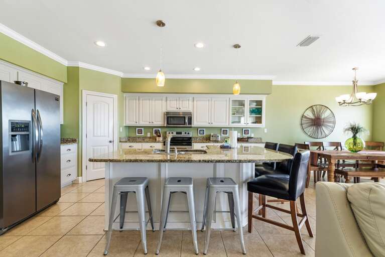 Kitchen features granite-topped island with metal stools, white cabinetry, stainless steel appliances, and green walls.