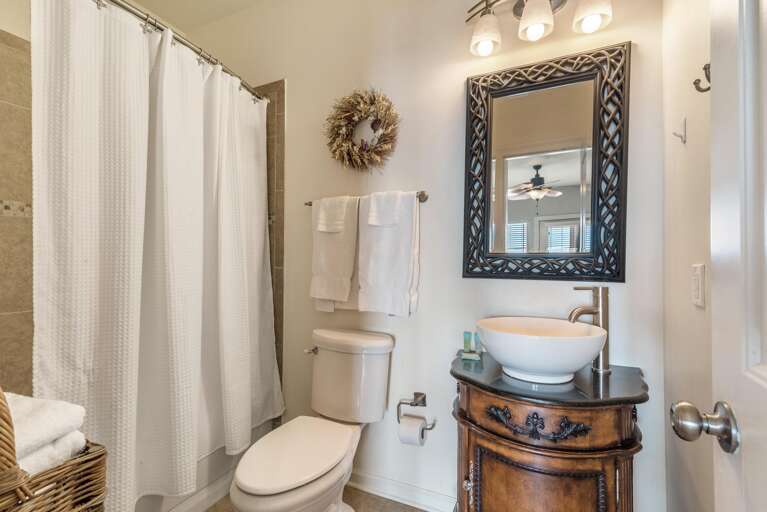 Bathroom with dark wood vanity topped by vessel sink, decorative framed mirror, and white textured shower curtain.