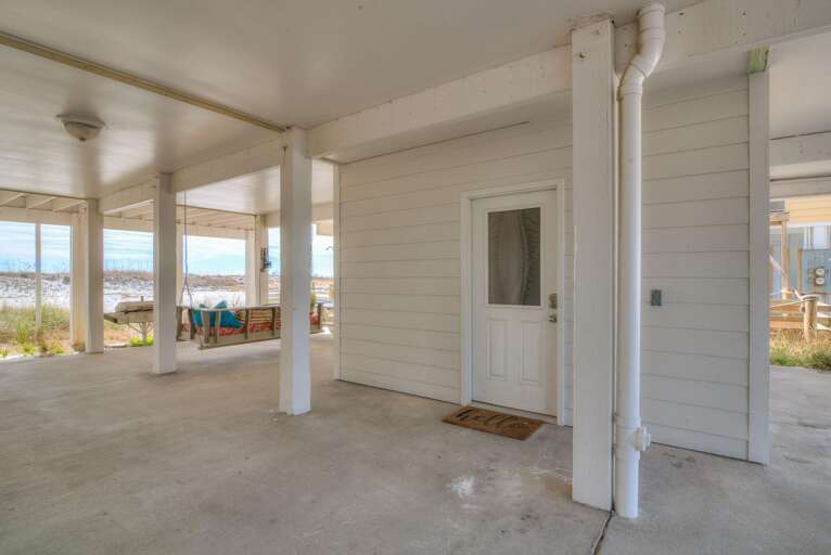 Concrete-floored covered area with white support columns, a glass-panel door, and a wooden porch swing with cushions.