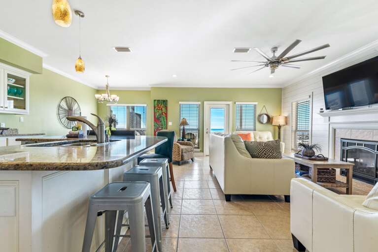 Tile flooring reflects natural light across the open living room and kitchen area with granite countertops and metal bar stools.