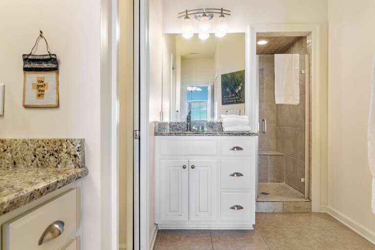 Bathroom features granite countertops, white cabinetry, a glass-enclosed tiled shower, and overhead vanity lighting.