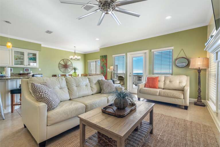 Green-painted living room walls frame cream leather sofas, a wooden coffee table with woven basket, and a ceiling fan above.