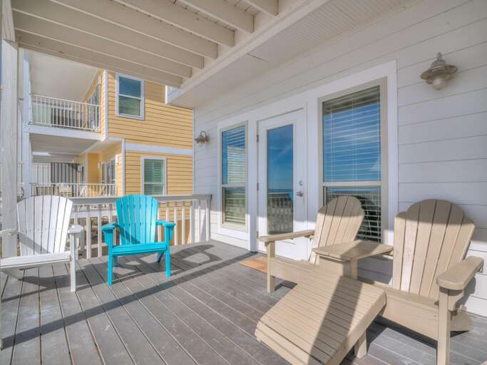 Living room features white-framed windows with blinds, flanked by glass door opening to a deck with Adirondack chairs.