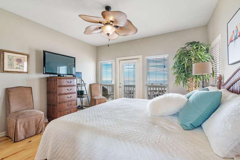 Bedroom features a wooden bed with white quilt, turquoise and white pillows, flanked by windows and balcony door.