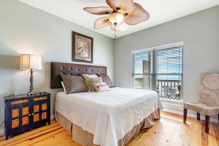Bedroom with natural wood floors, leather headboard, textured chair, and window offering balcony and Gulf views.