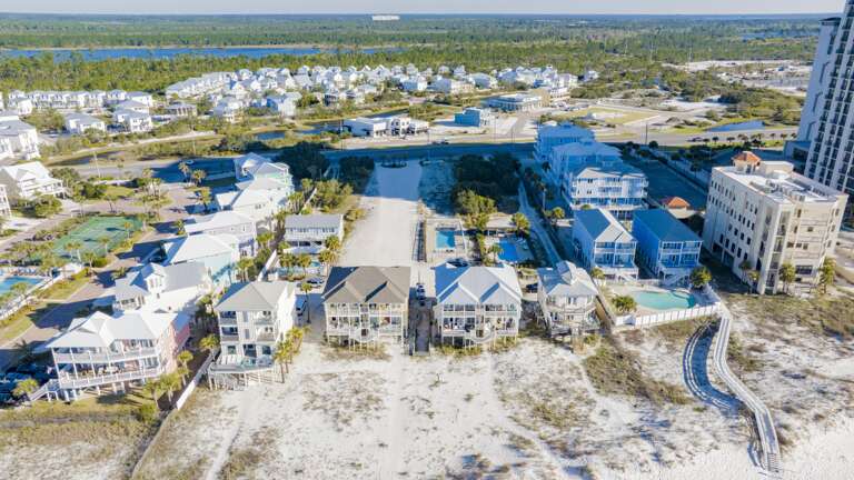 Front row of elevated homes features spacious screened balconies and staircases leading down to sandy dunes.