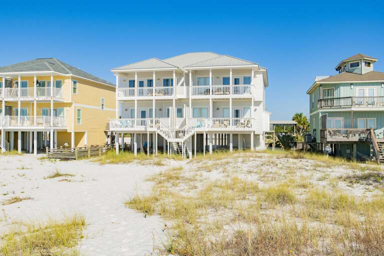 Triple-section white porch with railings and stairs leading down to sandy dunes and beach grass.
