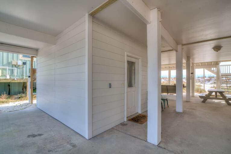 Covered concrete patio area with white support columns, picnic table, outdoor chairs, and sandy dune views.