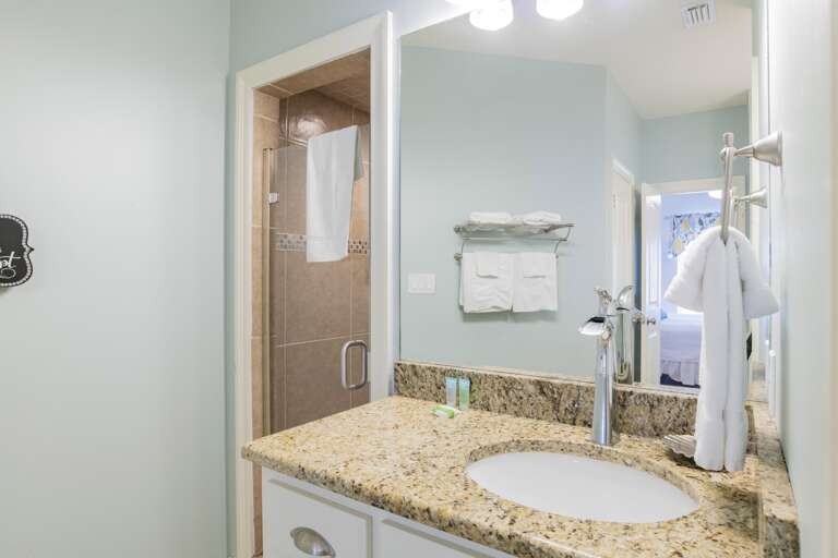 Light blue walls and a large mirror frame the granite vanity topped with folded white towels and toiletries.