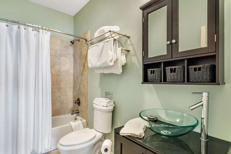 Tiled bathtub and shower combination with brushed metal fixtures and white fabric curtain on curved rod.