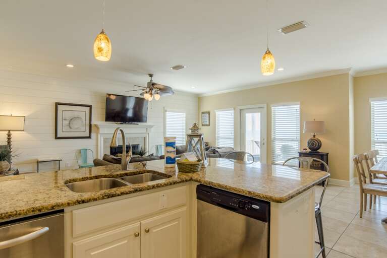Granite kitchen island with double sink and stainless steel dishwasher under amber pendant lights.