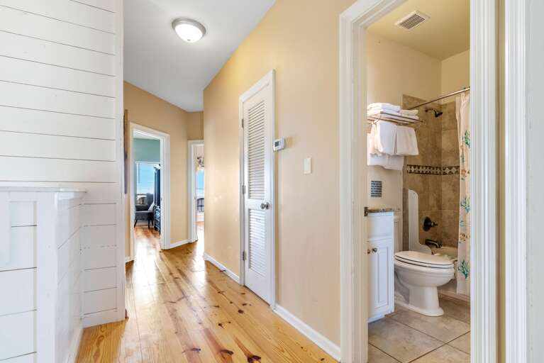 Bathroom features tiled shower surround with decorative border, white vanity, and folded towels on metal rack.