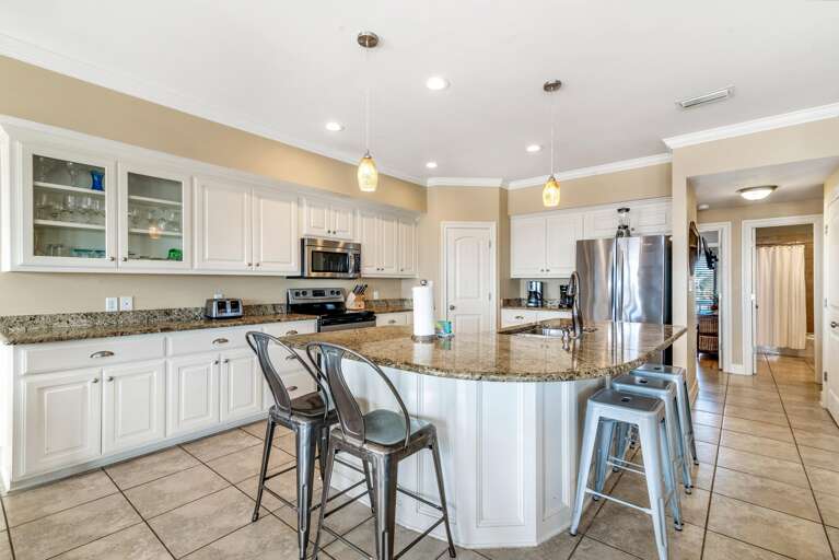 L-shaped granite island includes a double sink and metal stools beneath amber glass pendant lights.